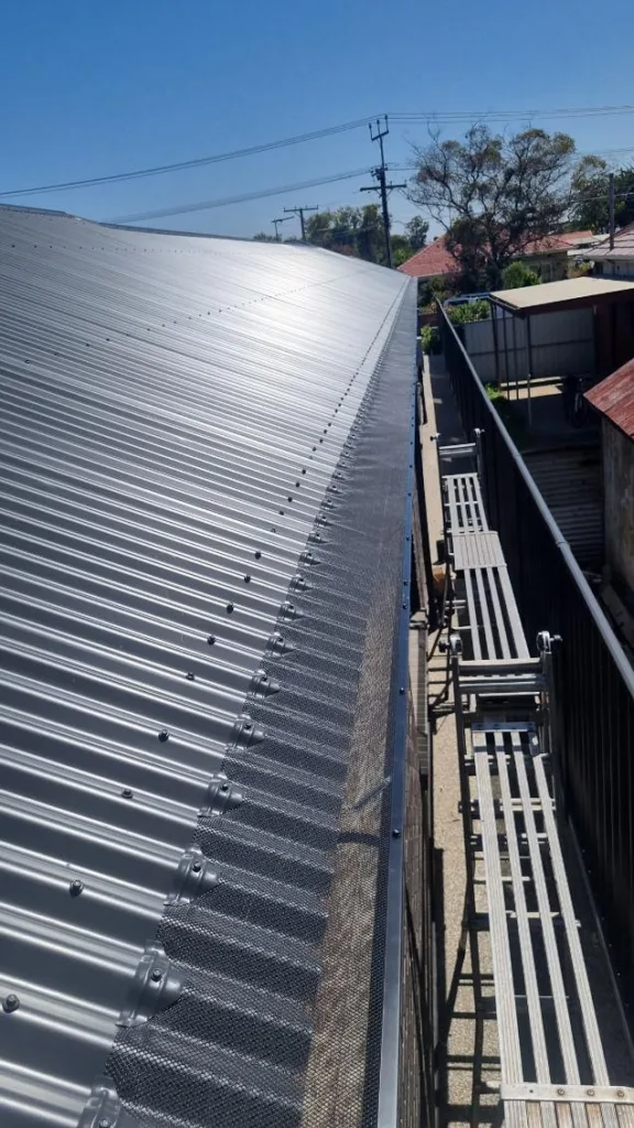 Long run of gutter guard mesh fixed along the gutter of a corrugated metal roof, installed by All Seasons Gutter Guard