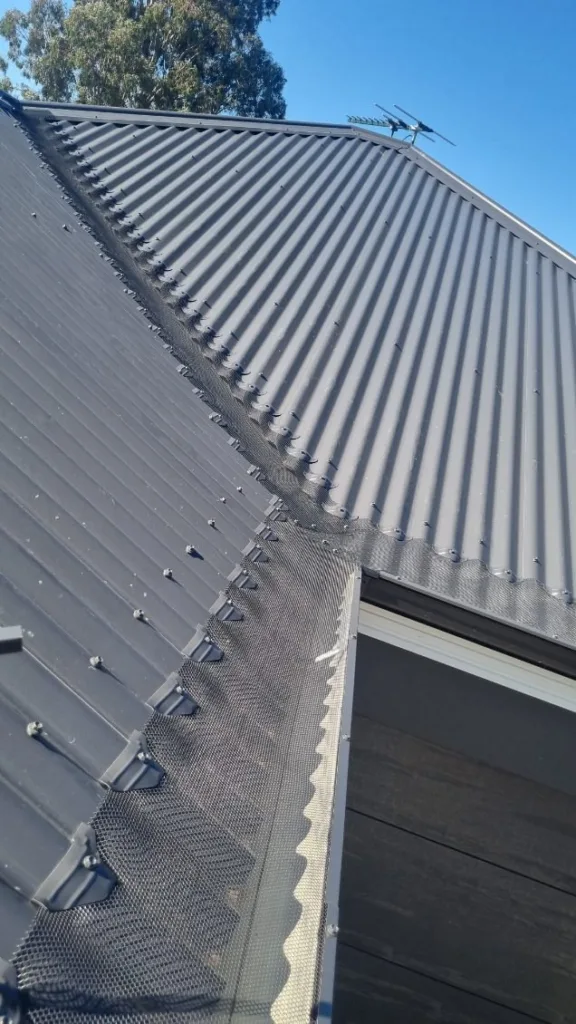 Gutter guard mesh covering a roof valley and the eaves gutter below it on a dark metal roof, installed by All Seasons Gutter Guard