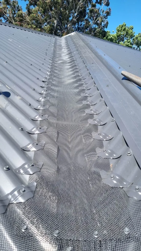 Roof valley on a corrugated metal roof fully covered with gutter guard mesh and secured with saddles on both sides, installed by All Seasons Gutter Guard
